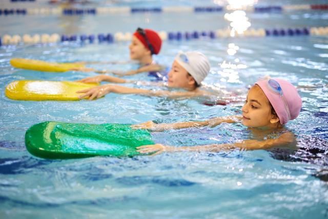 Drei Kinder lernen Schwimmen mit Schwimmbrett im Hallenbad
