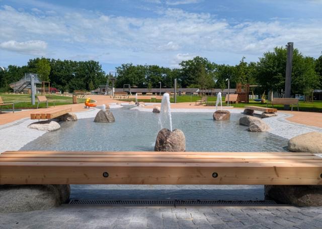 Flaches Naturfreibad mit Holzbank und sprudelnden Steinen im Becken
